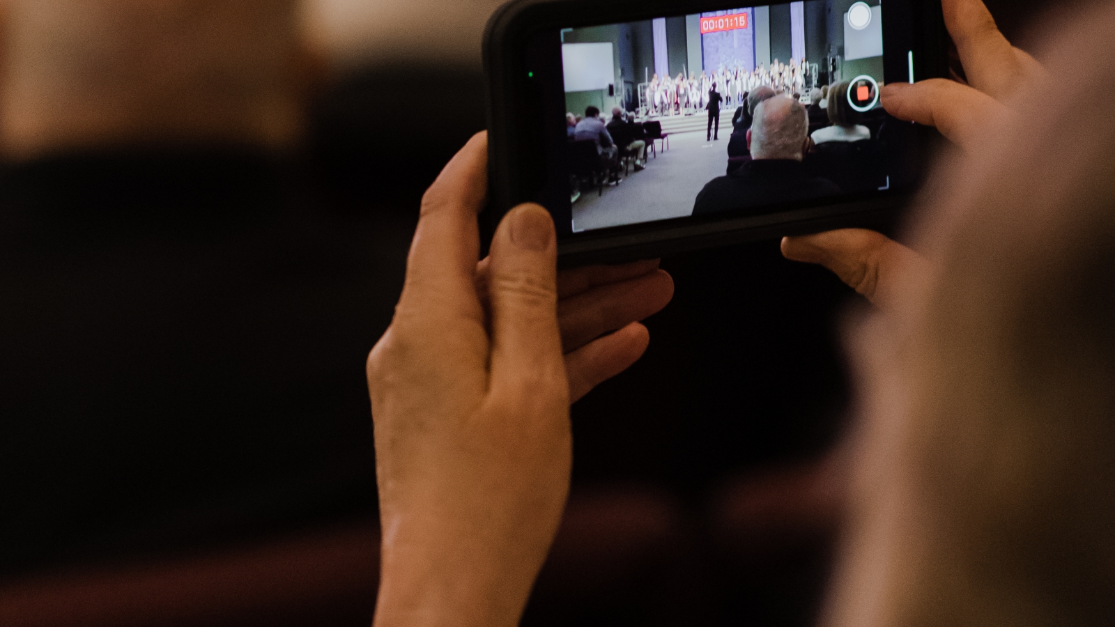 Member of audience holding up phone to take a picture of the choir performing.